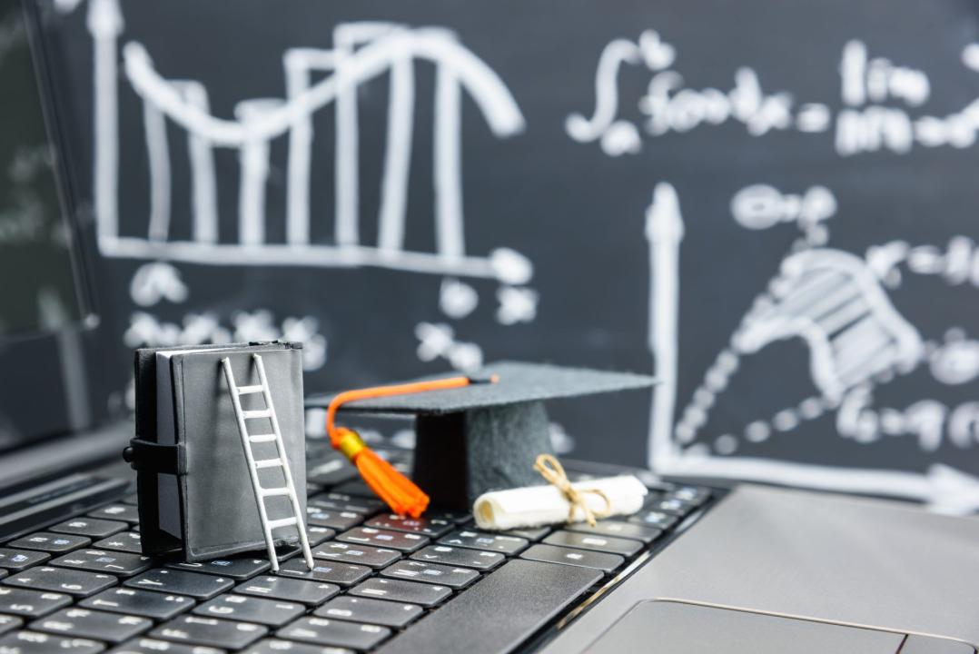 keyboard with mini graduation cap, diploma, and ladder leaned against book