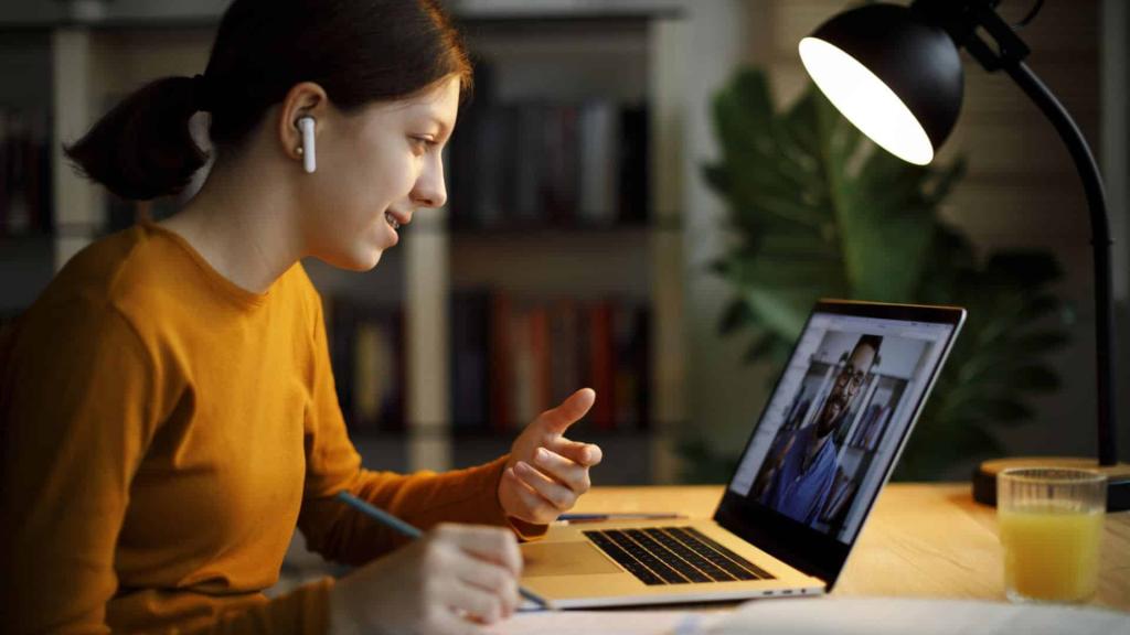 Smiling teenage girl with bluetooth headphones having video call on laptop computer at home