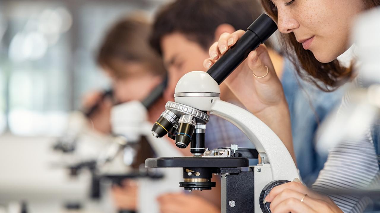 High school girl looking through microscope at school